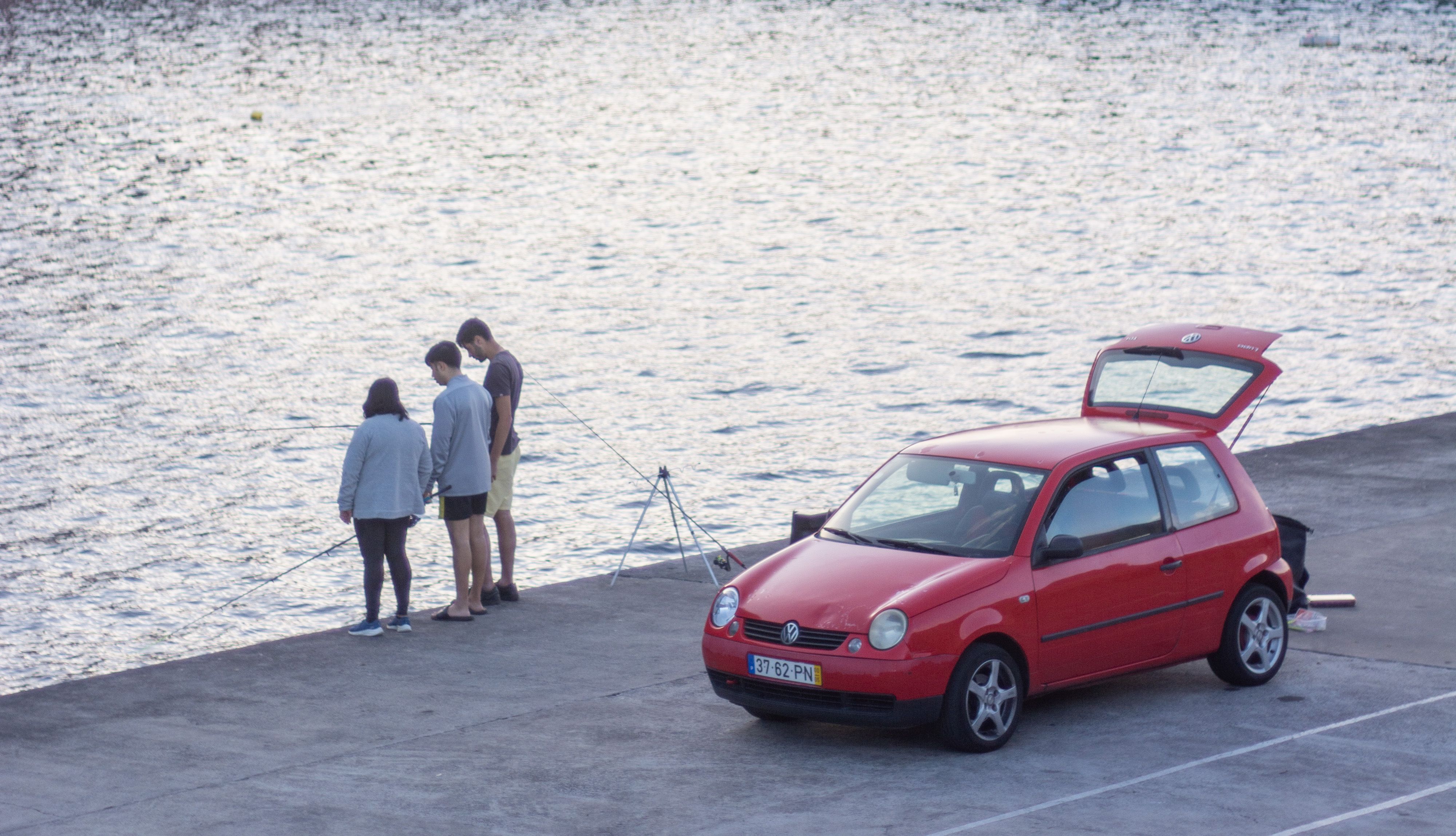 Drei Menschen stehen im Hafen und Angeln vor einem roten Auto