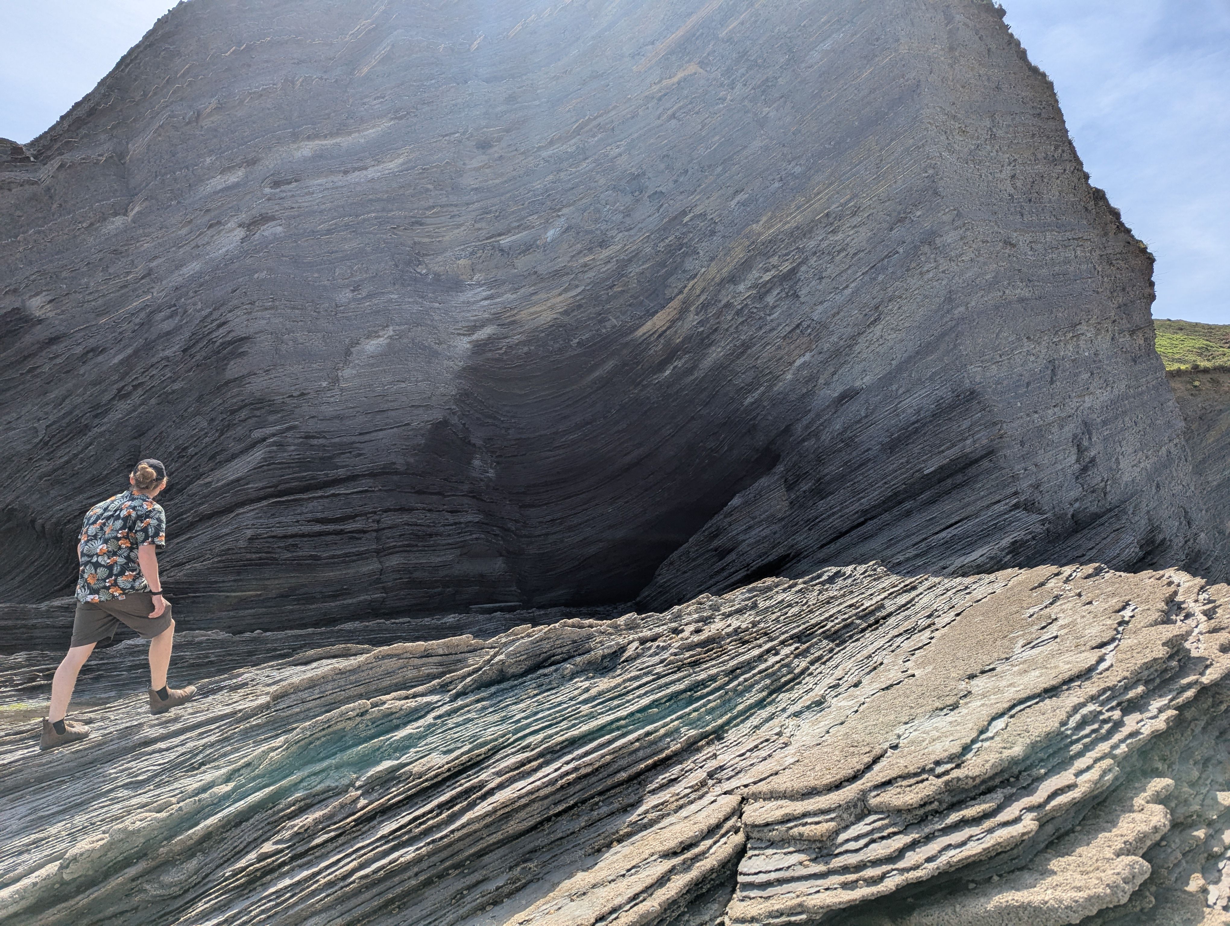 A person on flysch rock in front of a cave at the sea